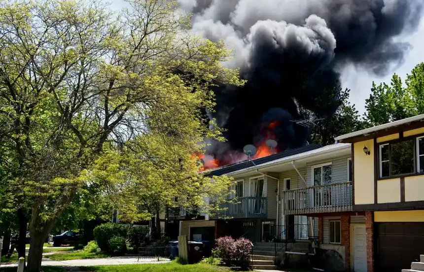 Dramatic house fire with thick smoke rising in a suburban neighborhood, surrounded by trees.