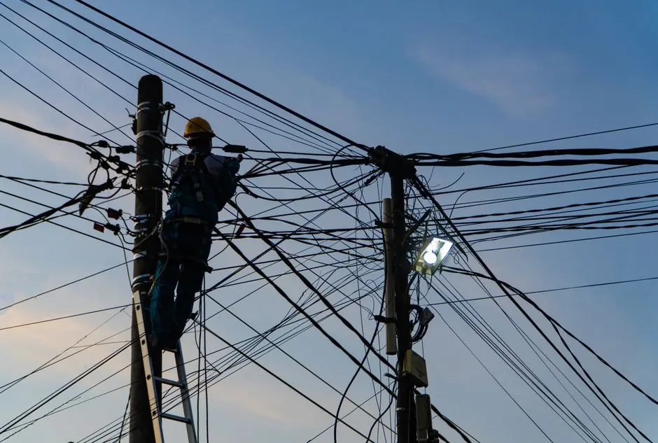 Silhouette of an electrician fixing power lines at sunset in Ubud, Bali.