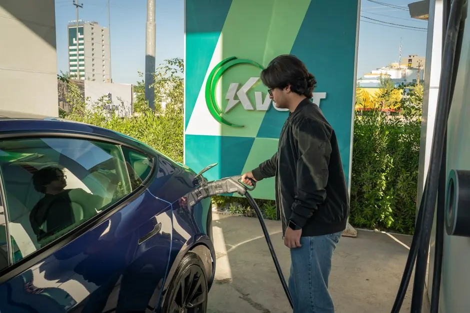 Young man charging a Tesla Model 3 at an outdoor electric vehicle station during the day.